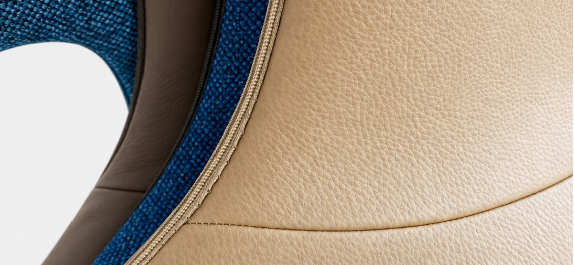 Detail of a chair upholstered in beige leather with a central seam, next to blue fabric with a pronounced weave