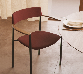 Perxa chair fully upholstered in burgundy, with exposed ash armrests and a black frame, beside a round table